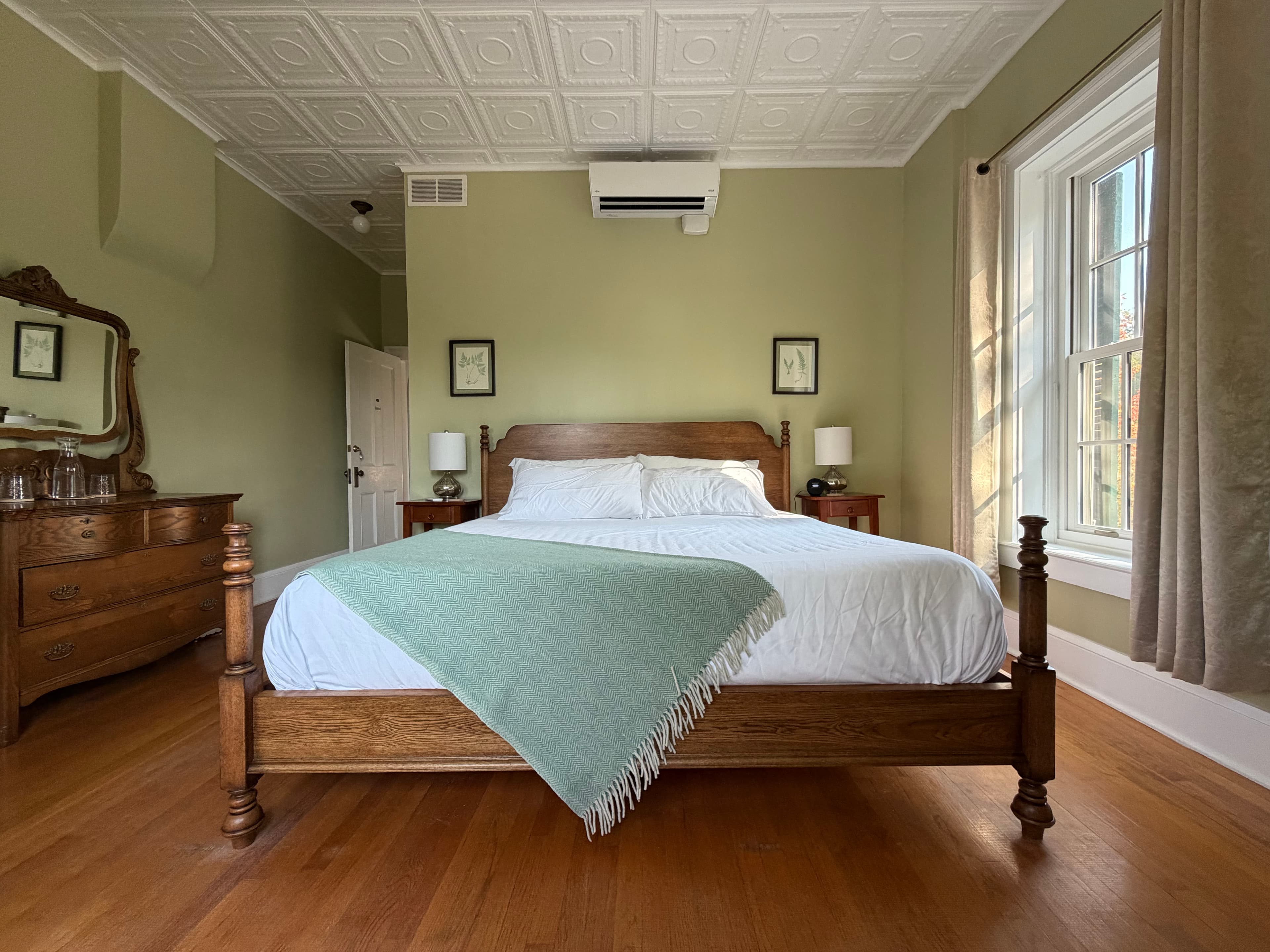 A spacious bedroom with light green walls, a gorgeous king-sized bed with brand new mattress and a tufted loveseat.