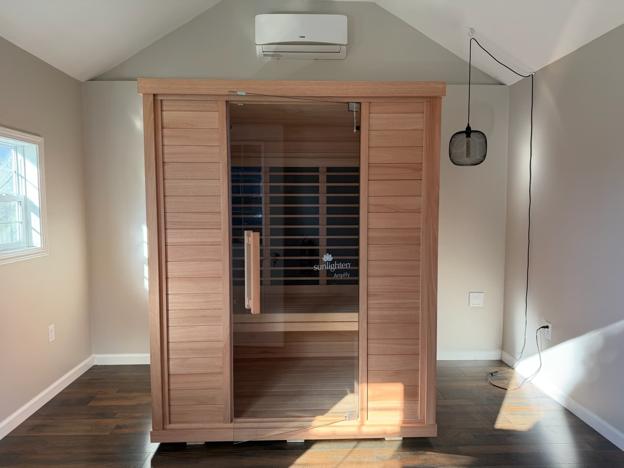 A wooden sauna with glass doors sits in a well-lit room with wooden flooring.