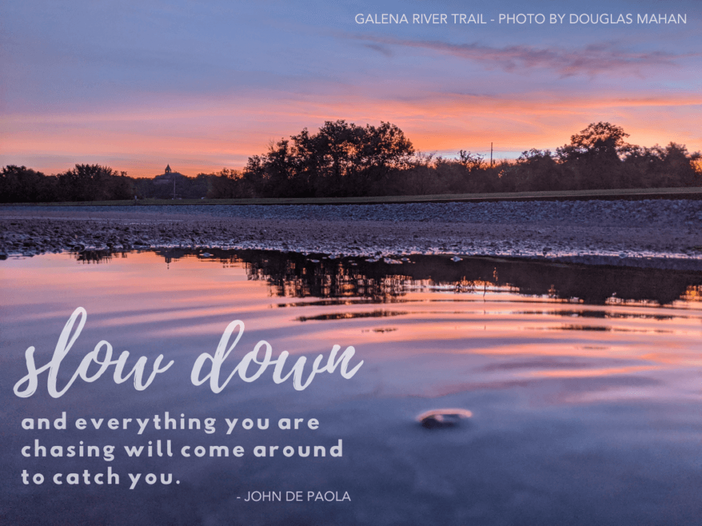 A serene sunset reflection on a trail with the quote "slow down and everything you are chasing will come around to catch you" by John De Paola.