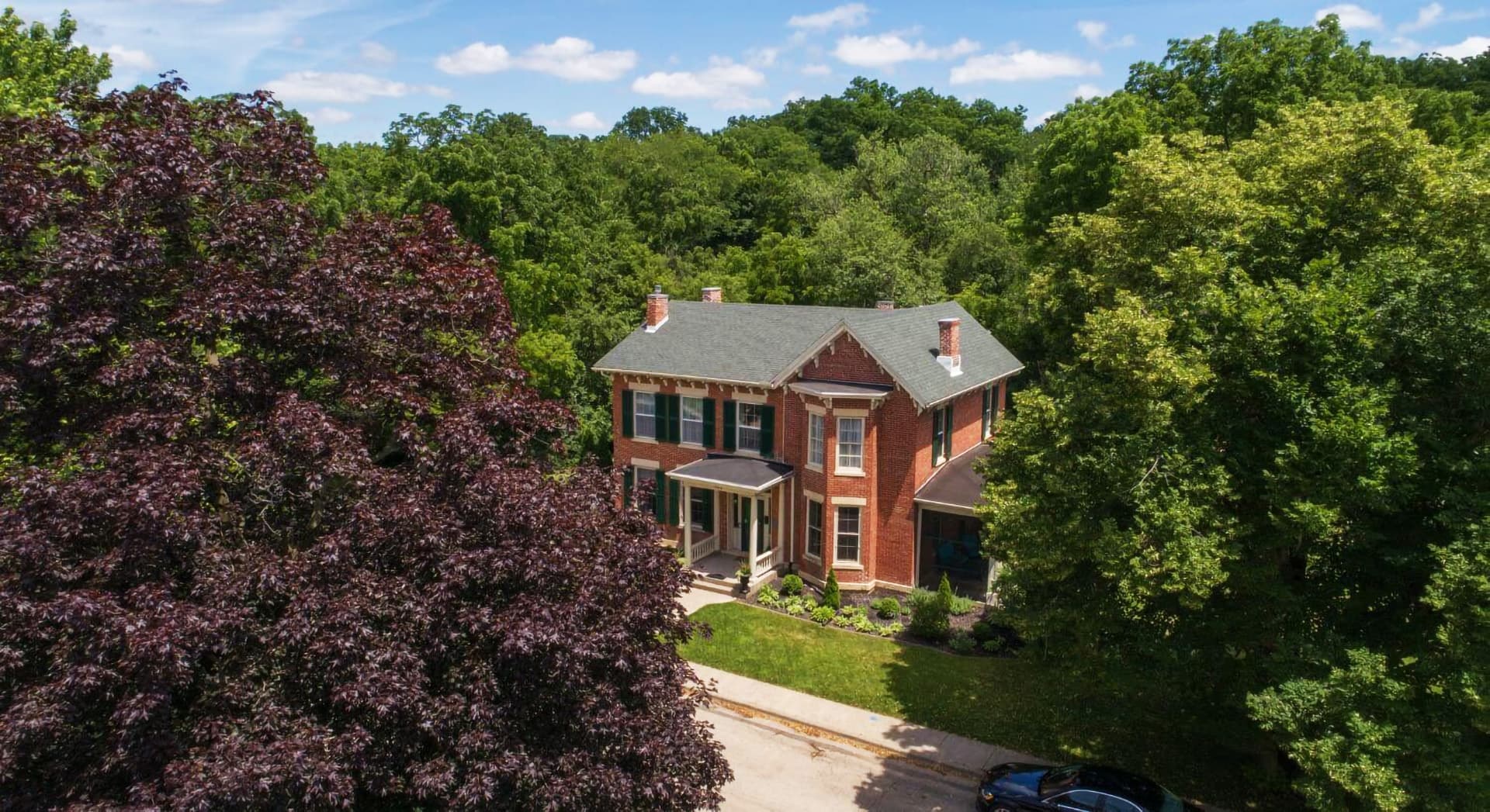 Aerial view of a large, red brick house surrounded by lush greenery.