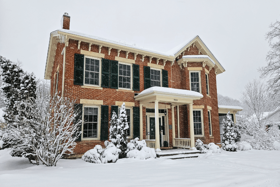 A brick house with green shutters surrounded by snow-covered landscapes.