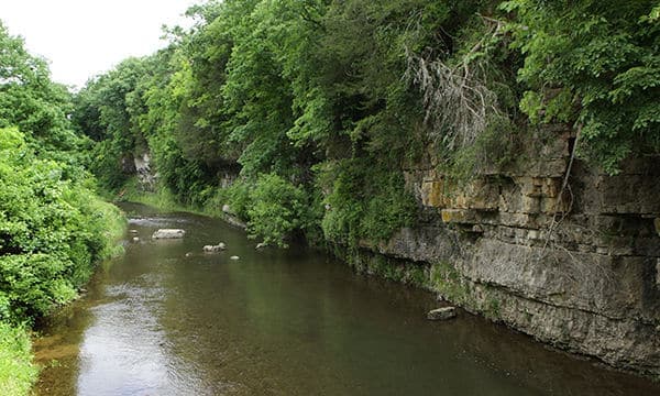 A serene river flows between lush green forested banks and rocky cliffs.