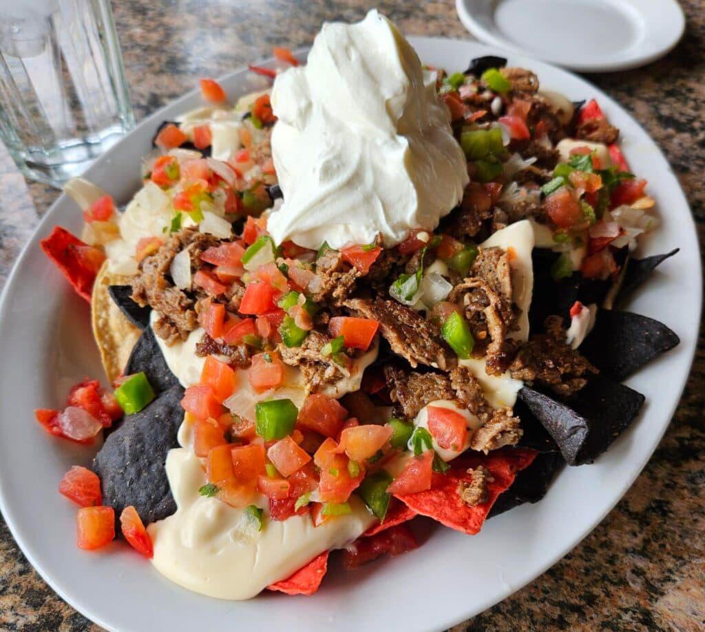 A plate of loaded nachos topped with ground beef, diced tomatoes, green peppers, onions, and a dollop of sour cream.