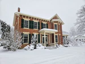 A brick house with green shutters covered in snow during winter.
