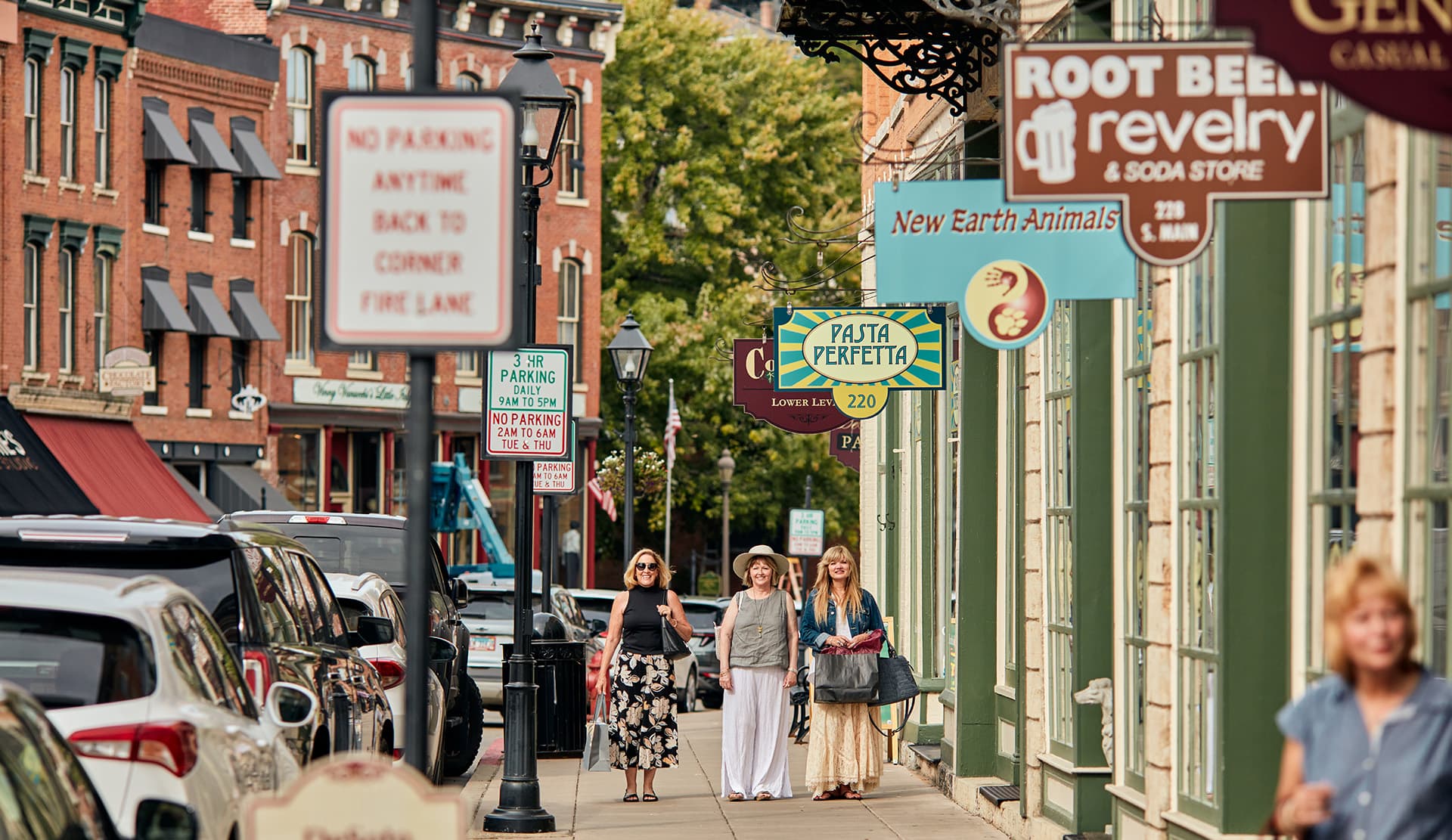 Three women stroll along a bustling city street lined with shops and signs.