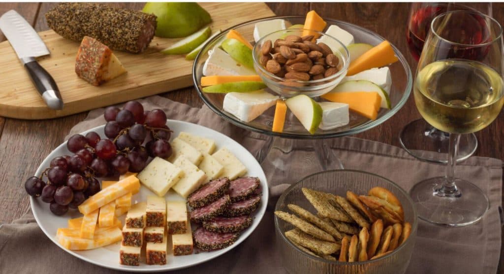 A variety of cheeses, meats, fruits, nuts, and crackers are arranged on a platter, accompanied by glasses of white and red wine.