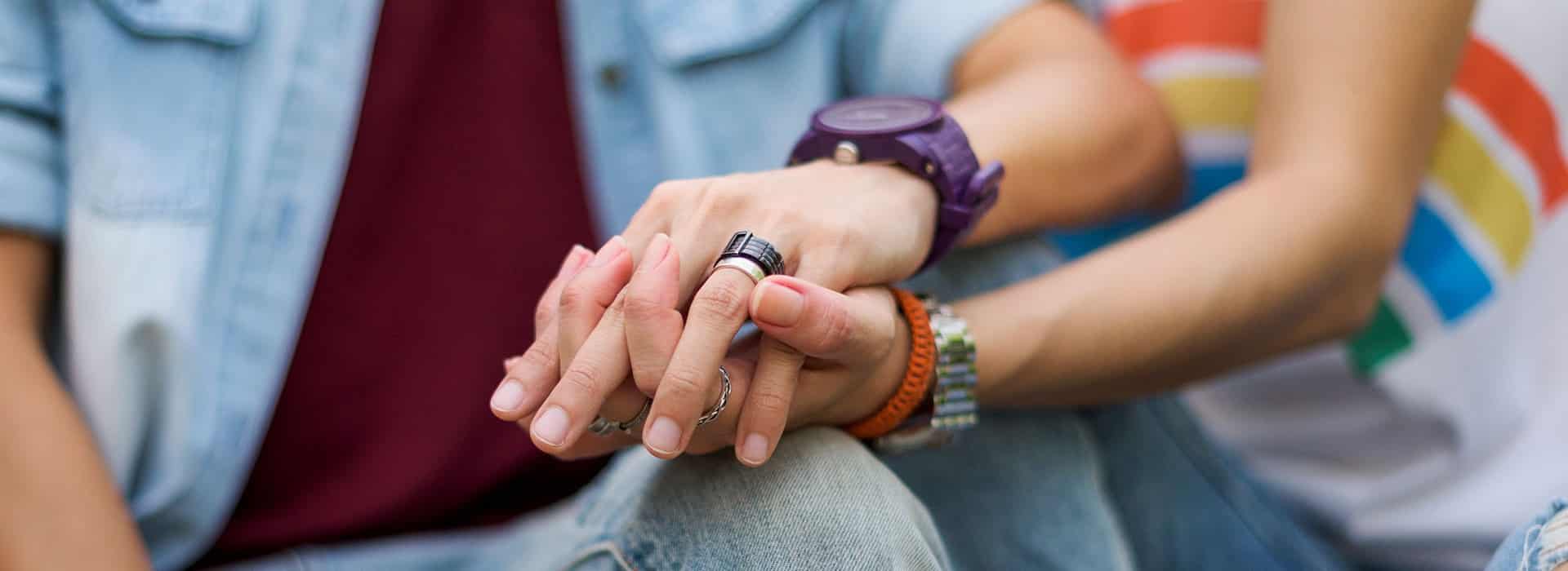 Two hands holding each other, adorned with rings, against a colorful background. Two hands holding each other, adorned with rings, against a colorful background.