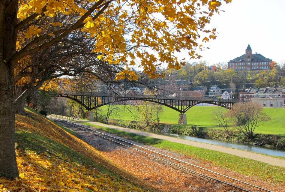 A scenic view of a bridge over a river, framed by golden autumn leaves and a hillside.