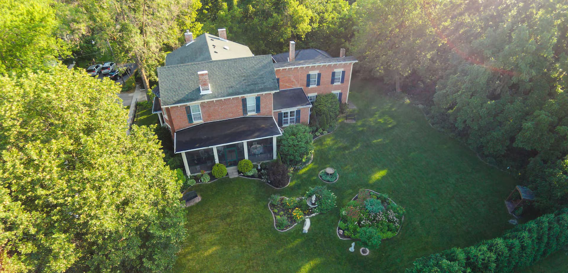 Aerial view of a brick house surrounded by lush trees and a landscaped yard.