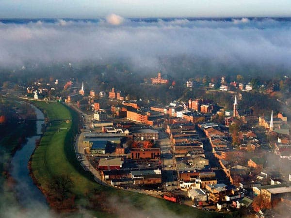 An aerial view of a small town partially shrouded in morning fog, with a river winding through it.