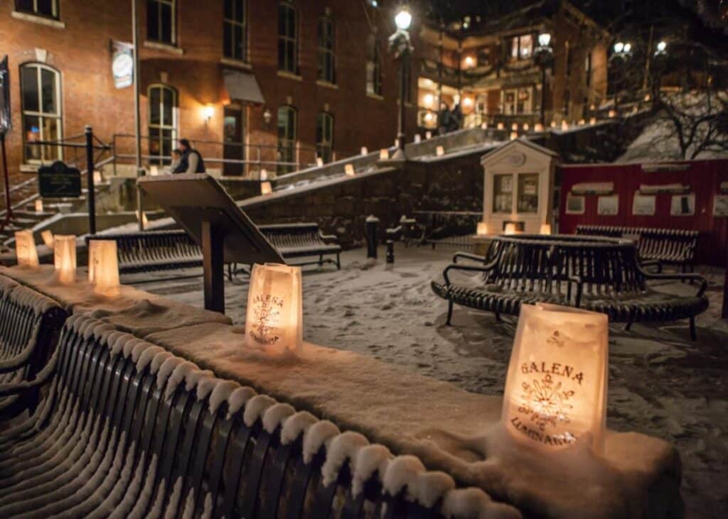 Snow-covered benches illuminated by lanterns in a charming town square at night.