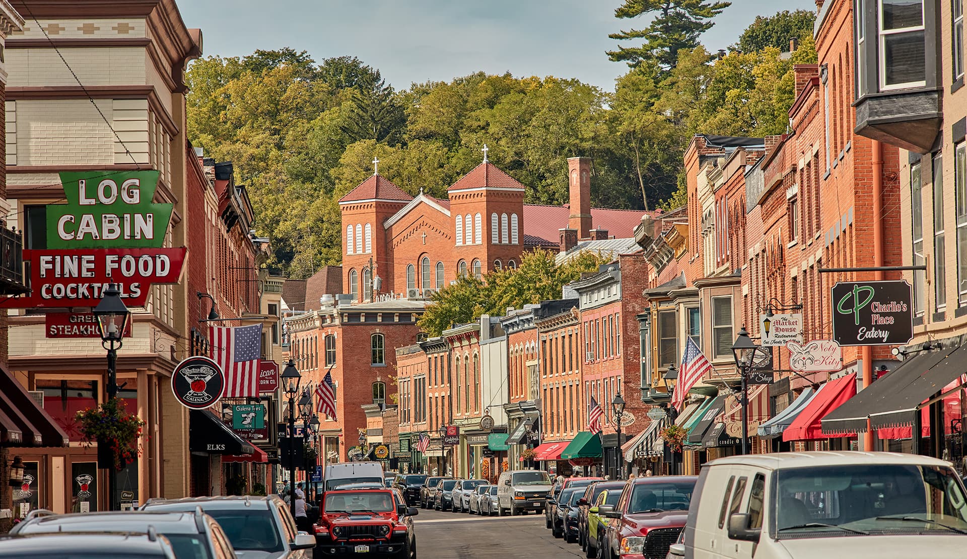 A bustling street lined with brick buildings, shops, and trees.