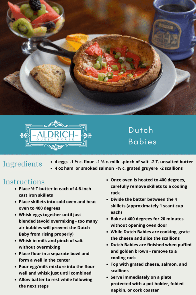 A plate featuring a Dutch Baby pancake topped with diced tomatoes and scallions, accompanied by a cookie and a fruit bowl, alongside a mug of coffee.