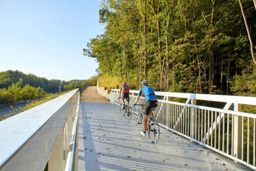 Two people riding bikes on a metal pedestrian bridge with railroad tracks to the left of them.