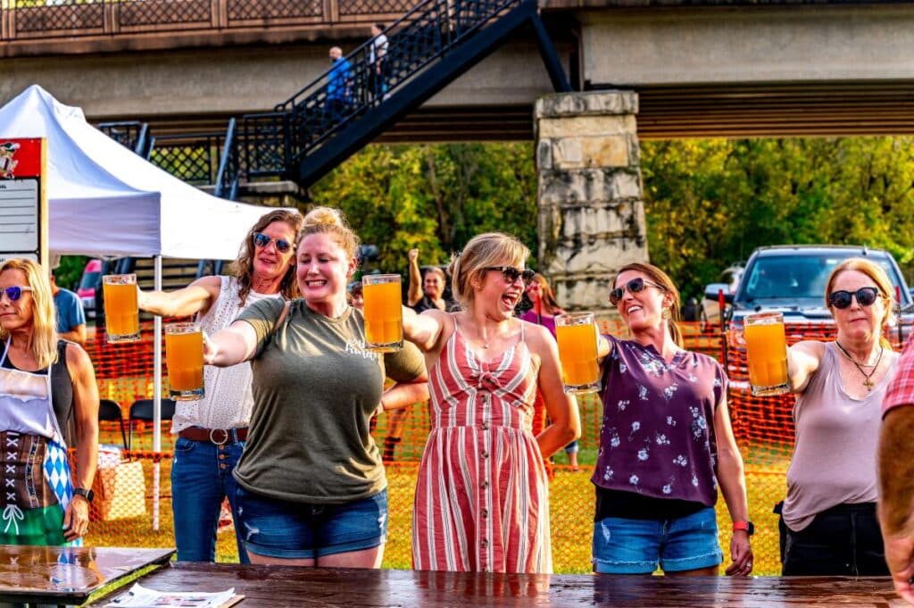 Five people hold steins of beer in front of them in a contest outside