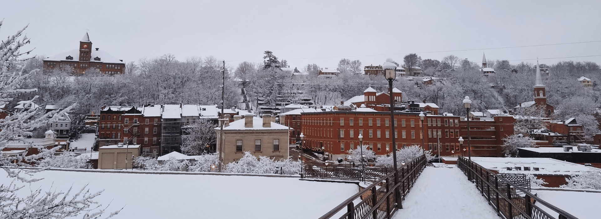 1850s brick buildings covered in snow seen from across a foot bridge