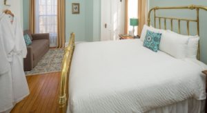 room with sage green walls, bed with brass head and foot rails, and white bedding, along with a green lamp and white robes