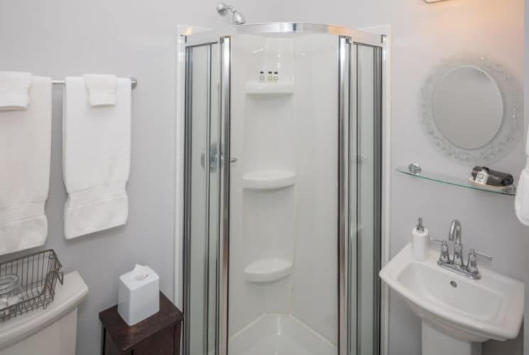 bathroom with white walls, a corner shower, white pedestal sink with mirror on the wall, a toilet, and white towels.