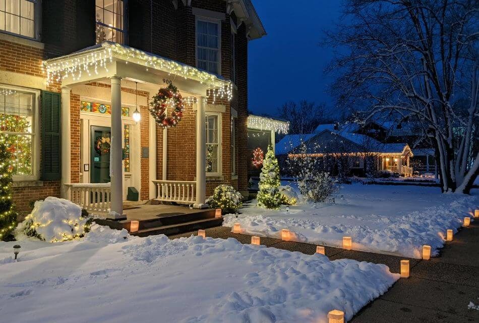 Christmas winter nights with house decorated and lit up, snow on the ground, a wreath hanging from the front, and luminaries adorning the walkway
