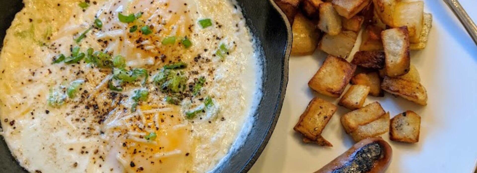 a black cast iron skillet with baked eggs inside, covered with bits of parmesan cheese, cracked black pepper, and chopped green onions, with a side of crispy golden potato pieces.