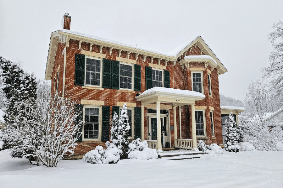 exterior shot of mid-1800s brick 2-story home covered and surrounded by snow