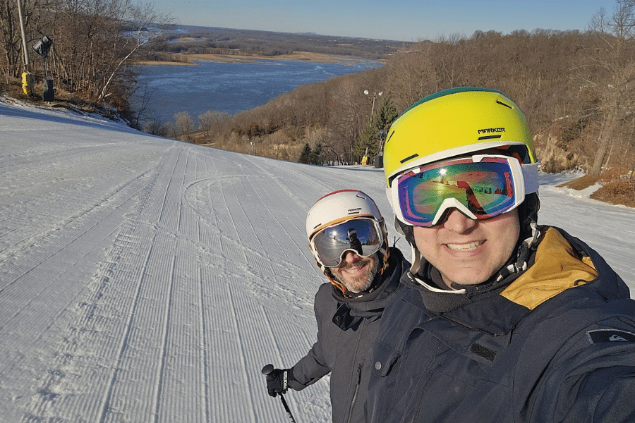 Two people dressed in ski gear at a ski resort with a river in the background